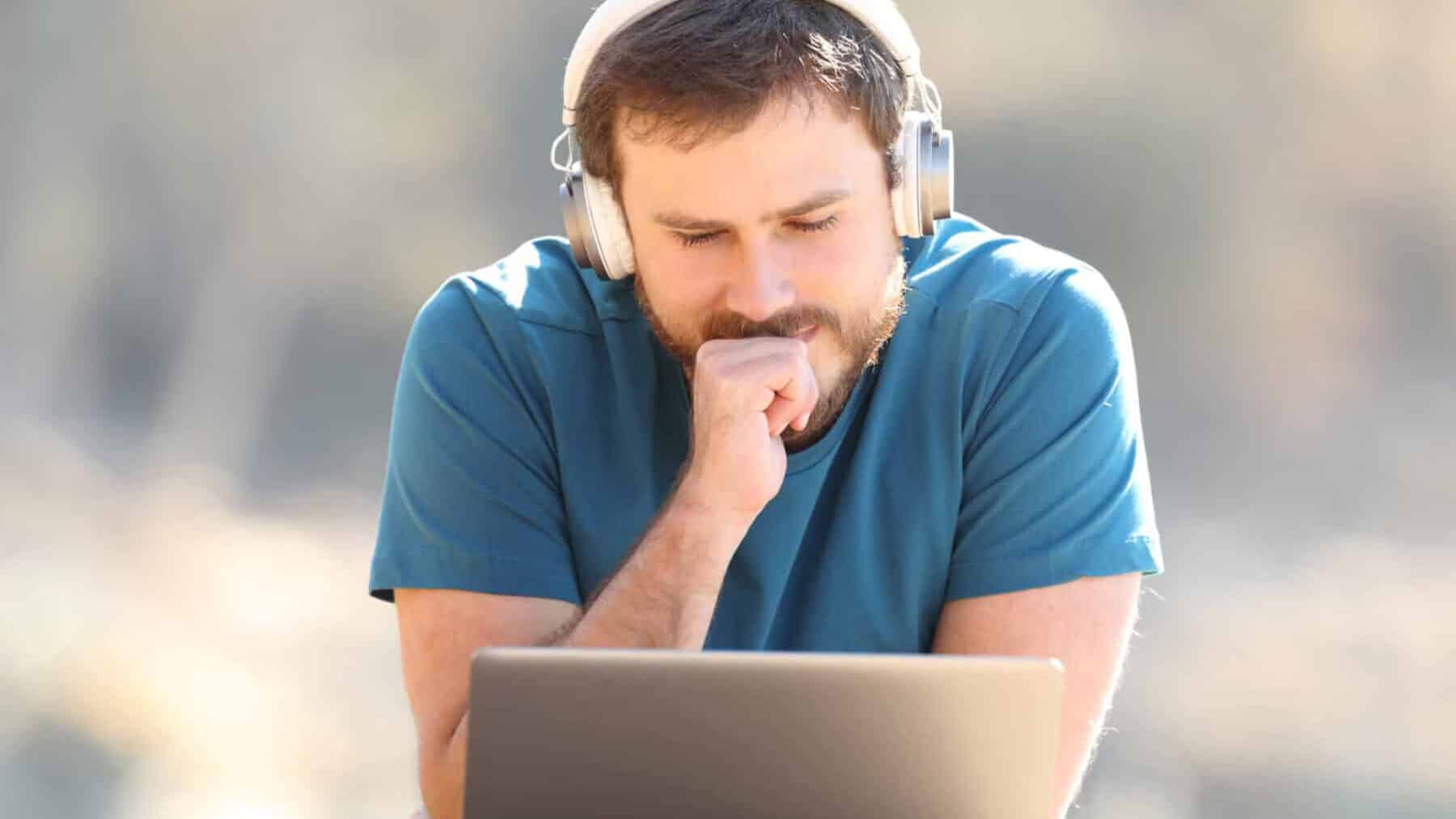 Mand med headphones kigger på åben laptop udenfor