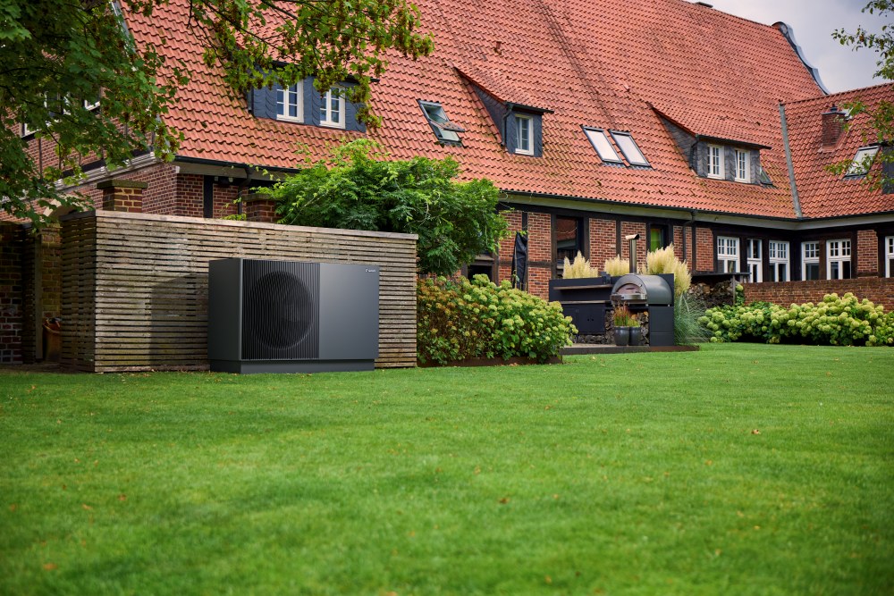Sort Vaillant aroTHERM perform varmepumpe på en græsplæne foran en stor murstensbygning.