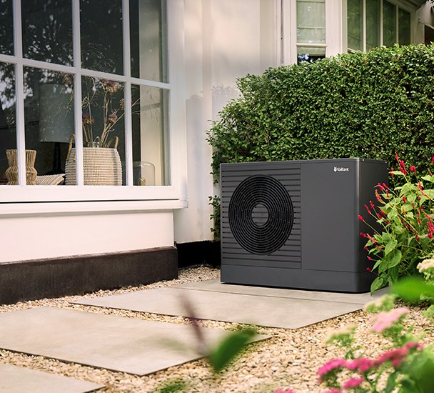 Sort Vaillant aroTHERM pro varmepumpe ved et hvidt hus og en grøn hæk.